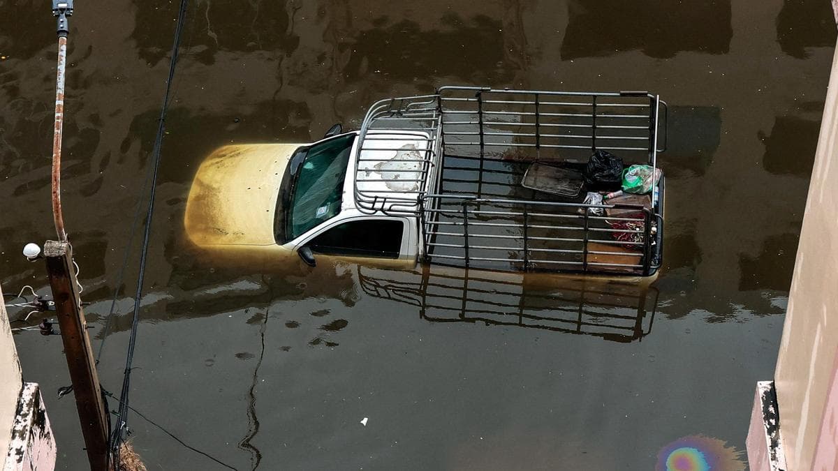 A white pickup truck submerged up to its windows in deep floodwaters seen from above.