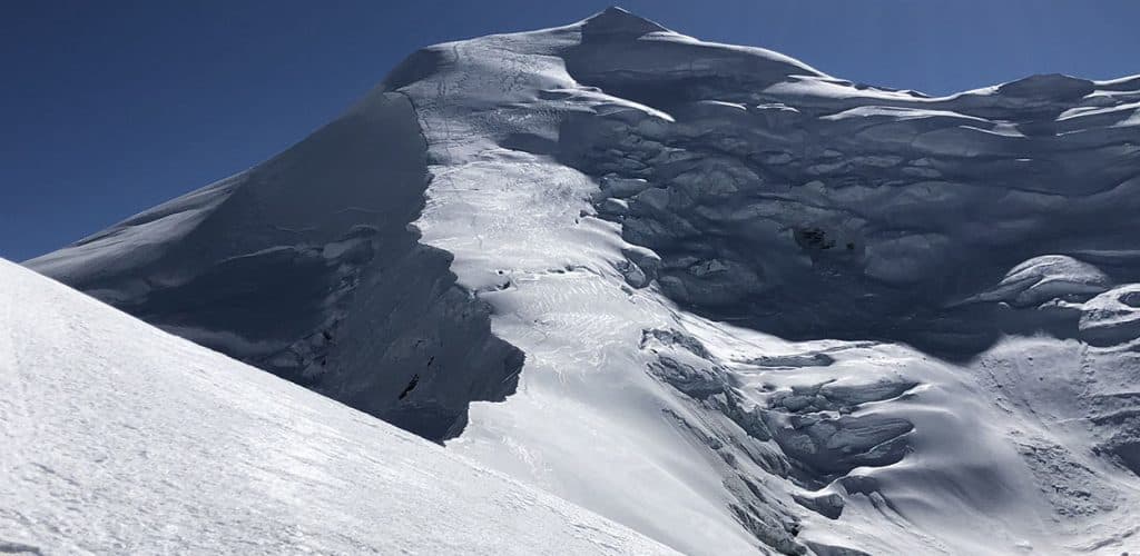 The snow-covered peak and icy slopes of Himlung Himal under a clear blue sky.