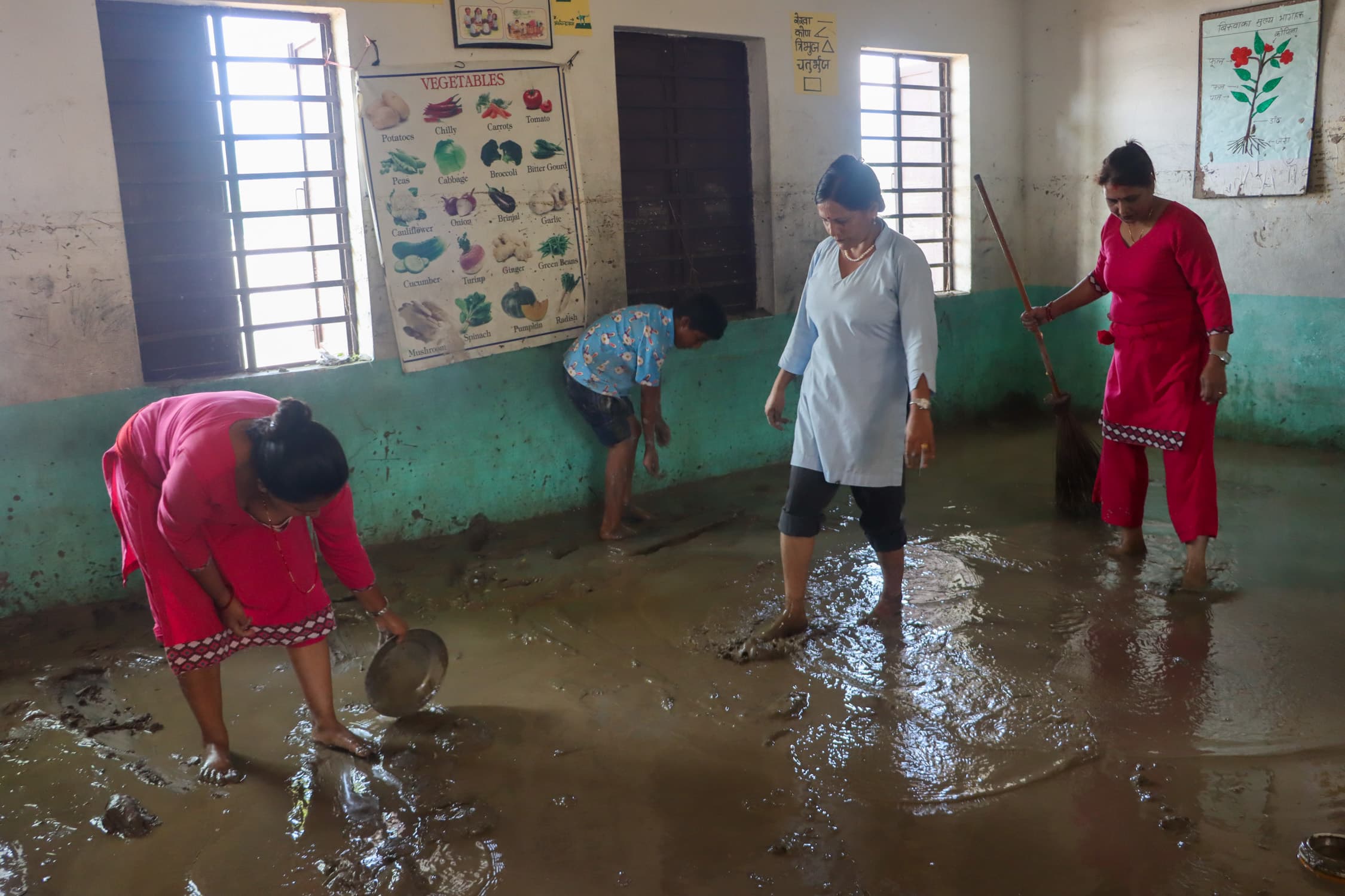 Staff and a pupil clearing thick river silt from a flooded classroom floor in Chitwan.