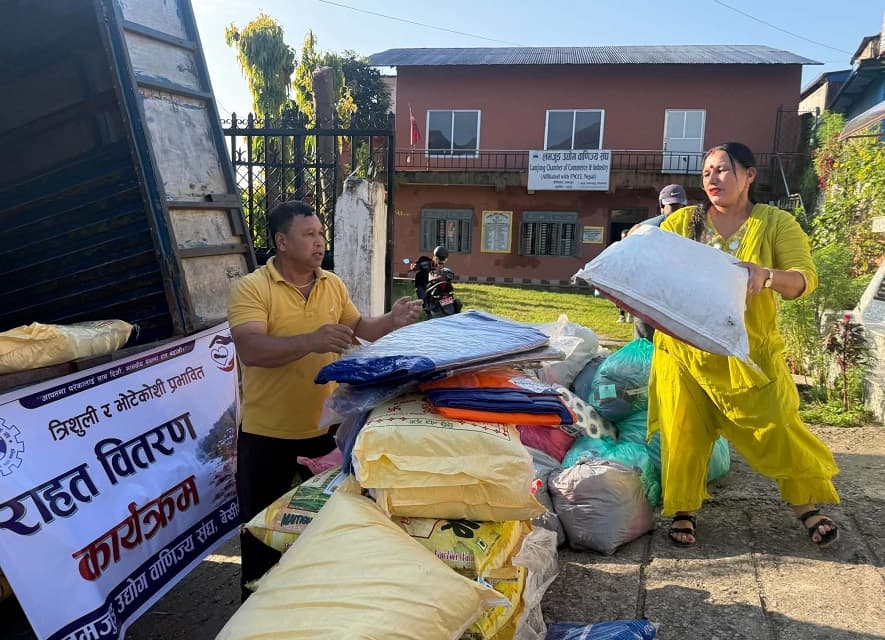 Workers load sacks of relief grain and tarpaulins beside a banner of the Lamjung Chamber of Commerce and Industry.