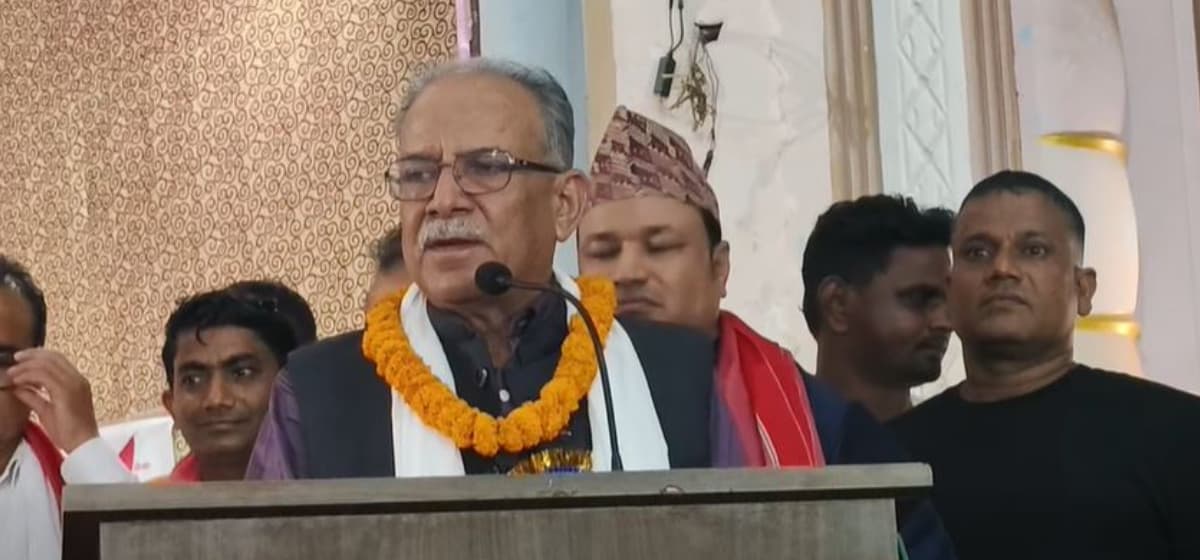 Pushpa Kamal Dahal wearing a marigold garland speaks into a microphone at a podium.