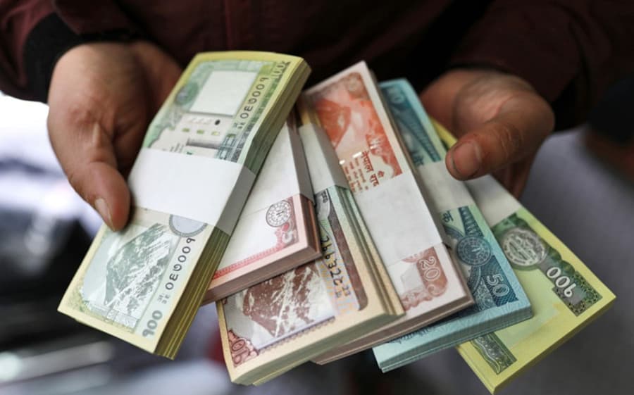 A person holding bundled packets of various denominations of Nepali rupee notes.