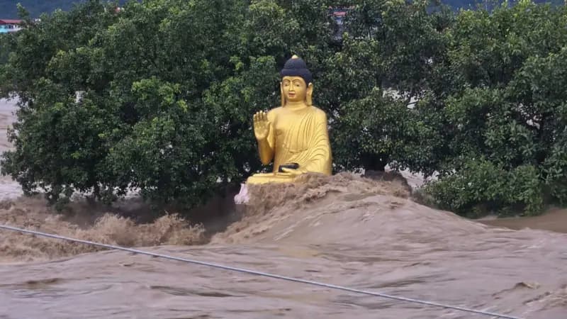 A golden statue of Buddha stands amid the roaring, muddy floodwaters of the swollen Narayani River.