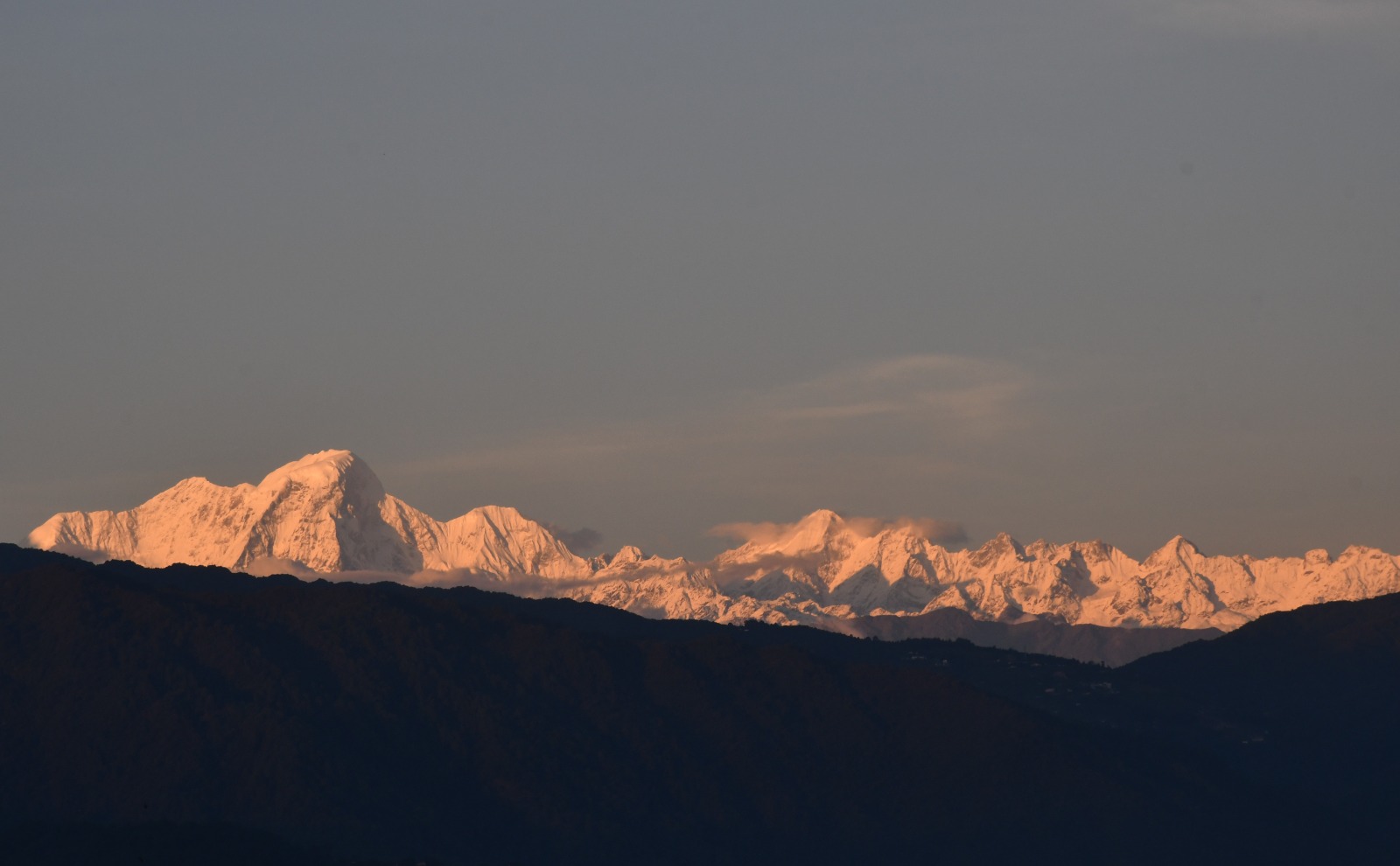 Snow-dusted Himalayan mountain peaks glowing in sunset light above hill ridgelines.