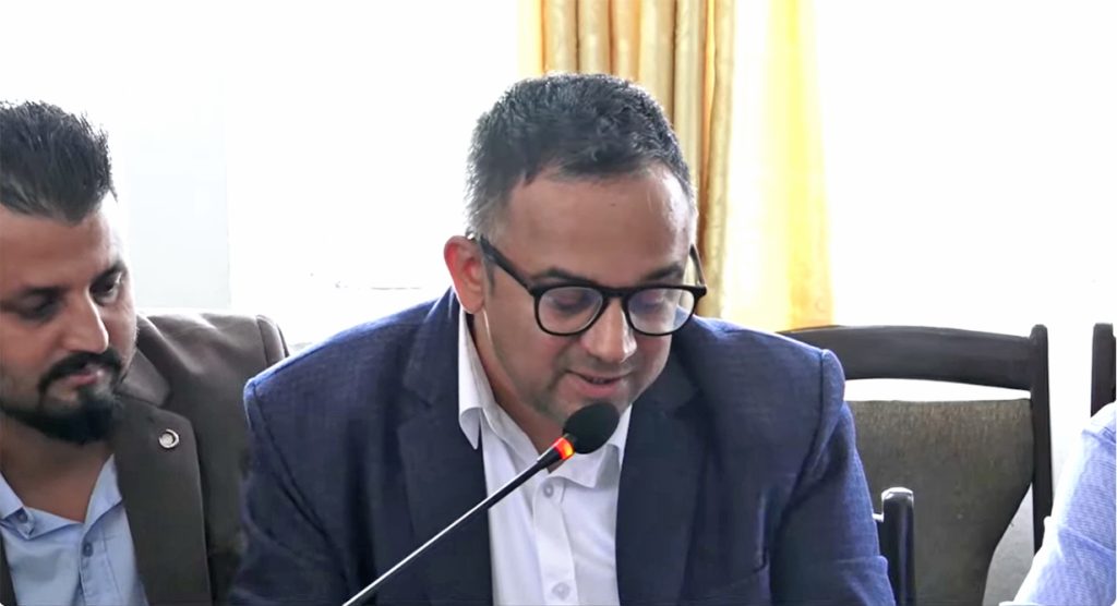 An investor association representative speaks into a microphone during a parliamentary committee discussion.