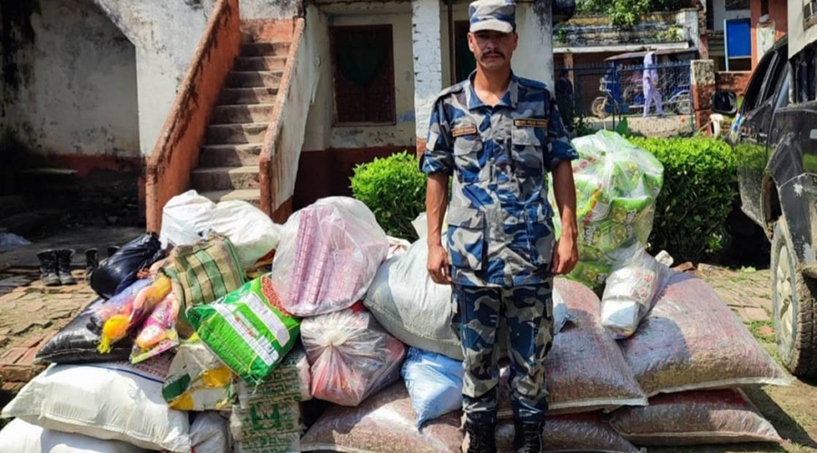 An Armed Police Force officer standing behind a pile of seized contraband goods and sacks in Siraha.